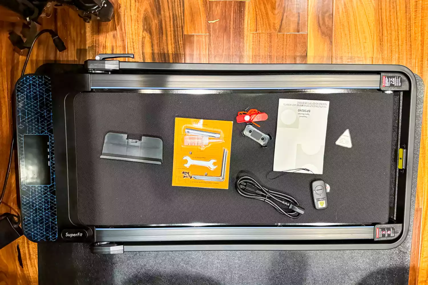 An overhead view of a treadmill belt with its manual, power cord, and safety accessories laid out.