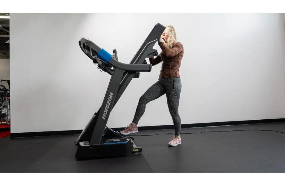 A woman easily folding the deck of a Horizon treadmill upwards for storage.