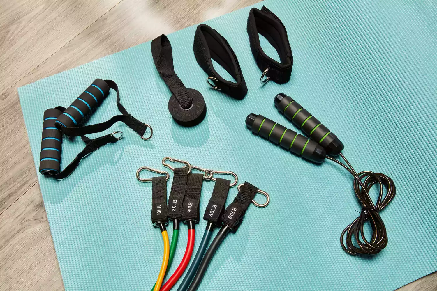 A resistance band kit with handles, ankle straps, and a jump rope laid out on a blue yoga mat.