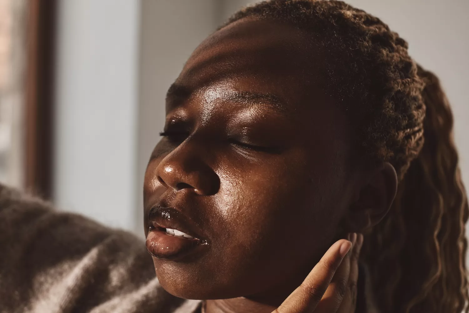 A person with eyes closed gently touching their ear in a moment of reflection or discomfort.