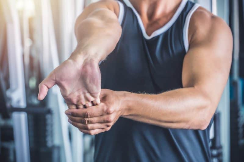 A man in a gym performing forearm stretches for elbow pain relief by extending his wrist.