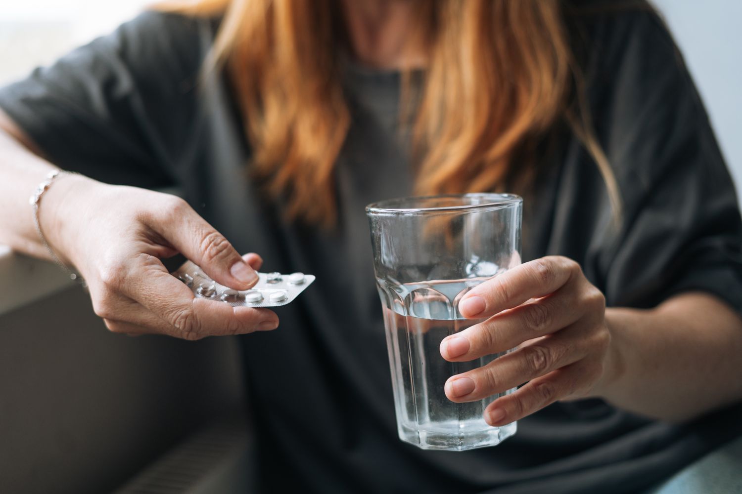 A woman holding a packet of cold medication and a glass of water.
