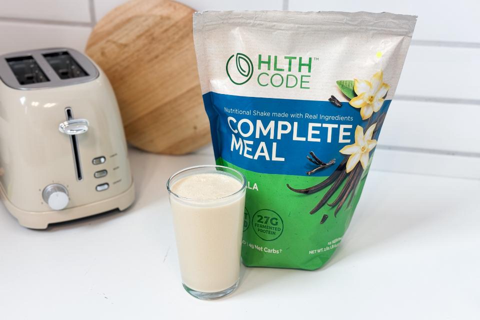 A person holding a HLTH Complete Meal replacement shake bag, showing its size and portability.