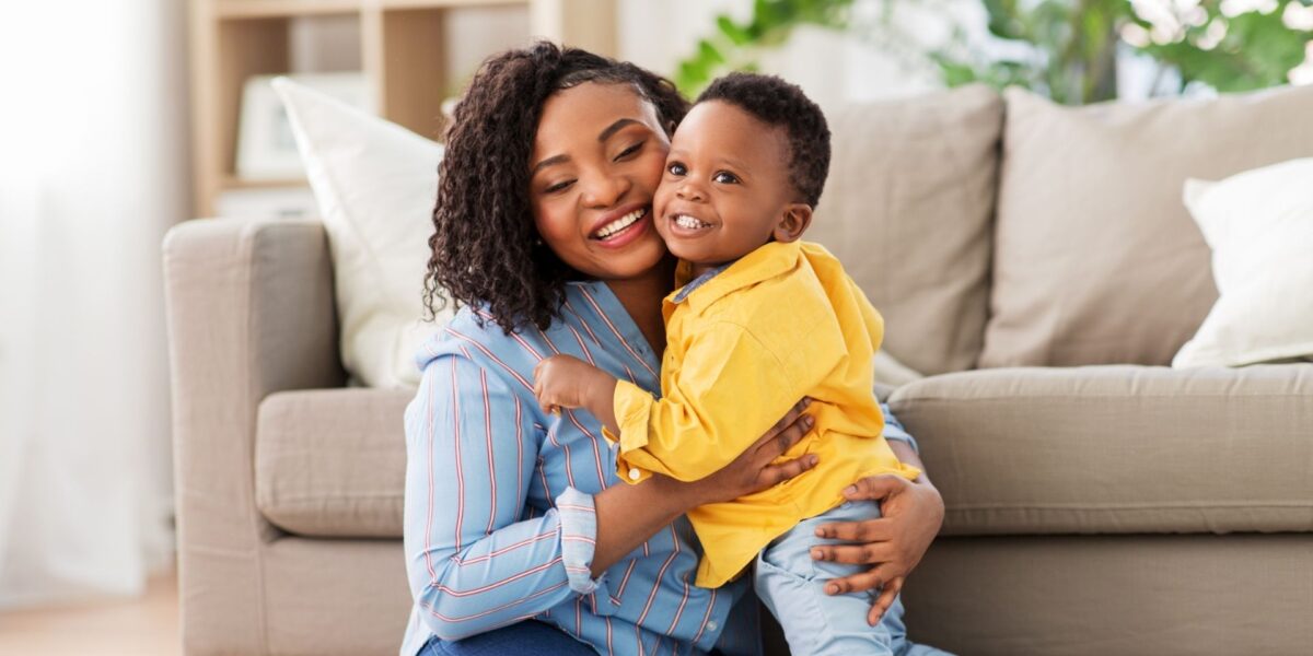 A smiling woman hugging a happy young child wearing a bright yellow shirt.