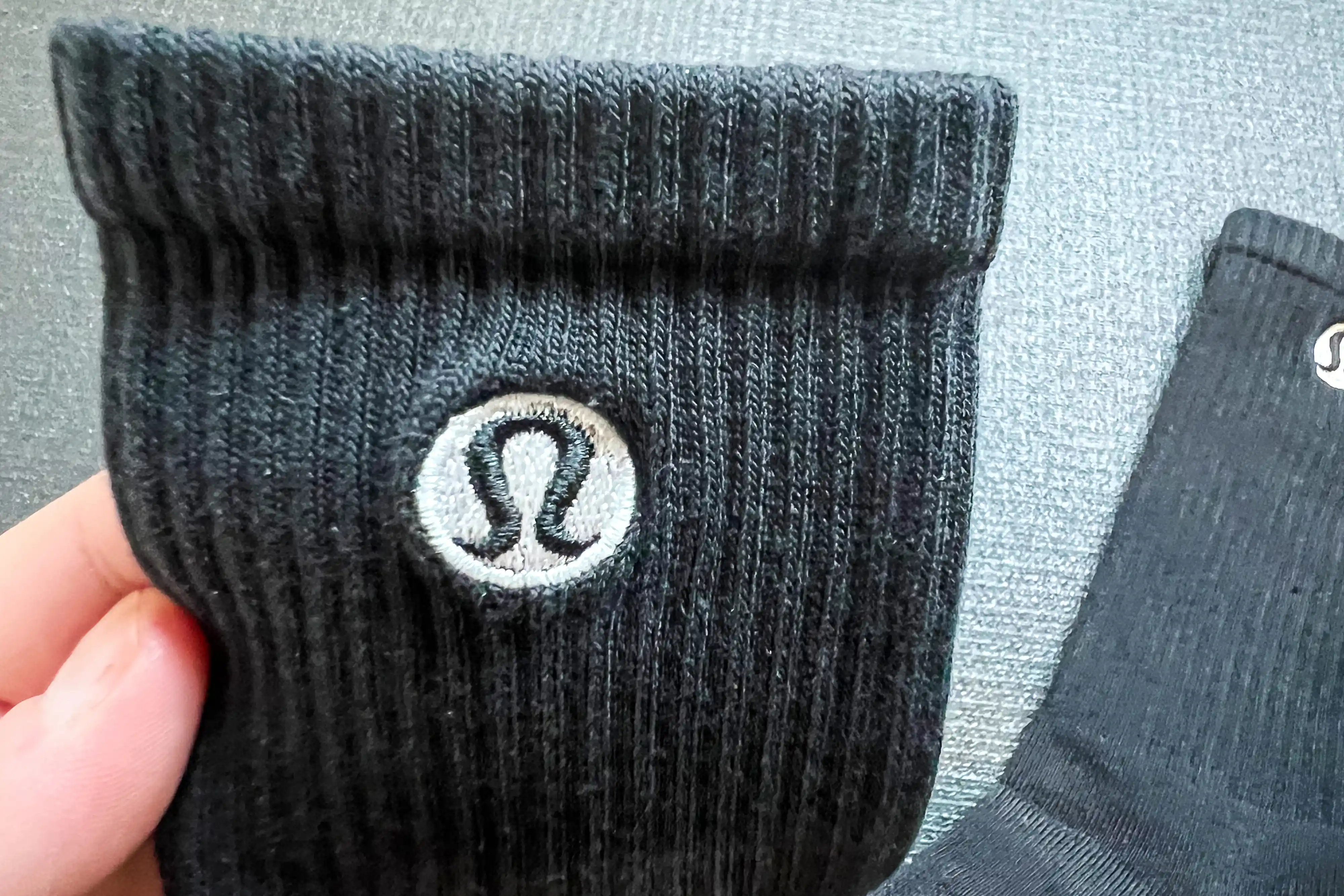 Close-up of a hand holding a black Lululemon ribbed crew sock showing the logo and knit texture.