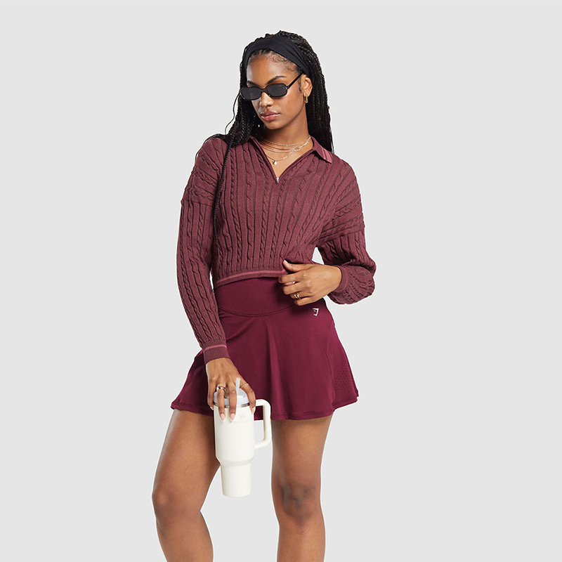 A preppy tenniscore outfit featuring a cable knit sweater draped over a skort.