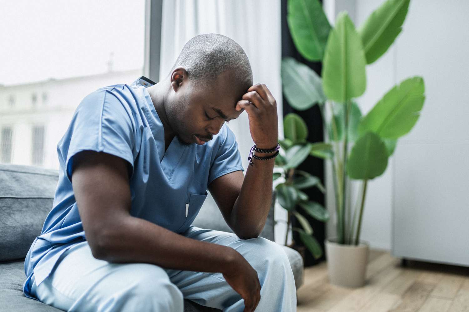 An exhausted nurse sitting on a sofa with eyes closed after a shift.