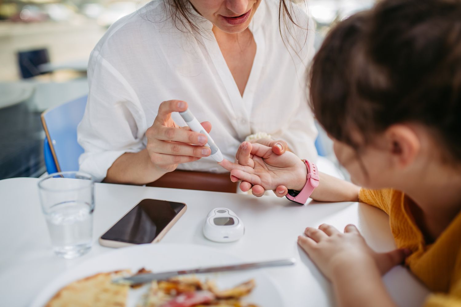 A mother performing a finger-prick blood glucose test on her young daughter.