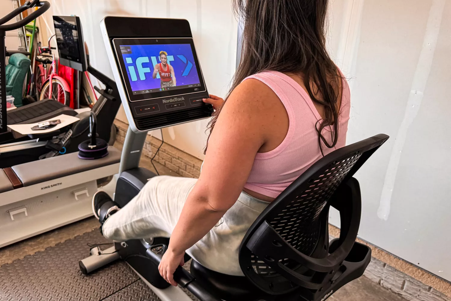 A person using a NordicTrack recumbent bike with a large touchscreen showing an iFIT workout class.