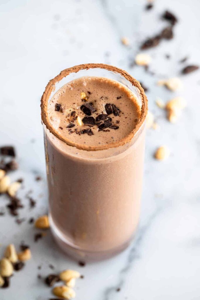 A peanut butter chocolate protein shake in a tall glass with a straw.