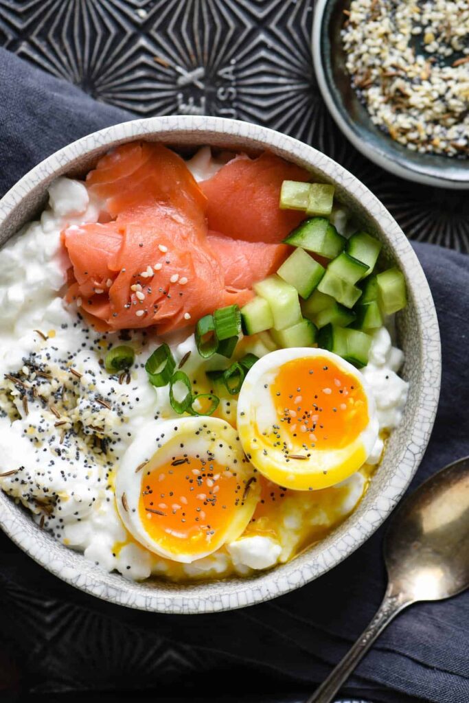 A savory cottage cheese bowl topped with sliced cucumbers, tomatoes, and herbs.