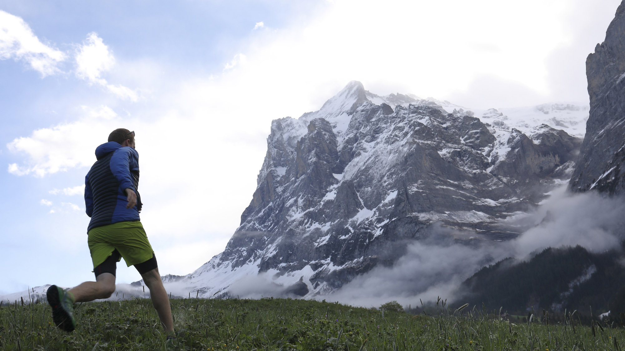 A runner approaching a mountain peak wearing a technical lightweight shell.