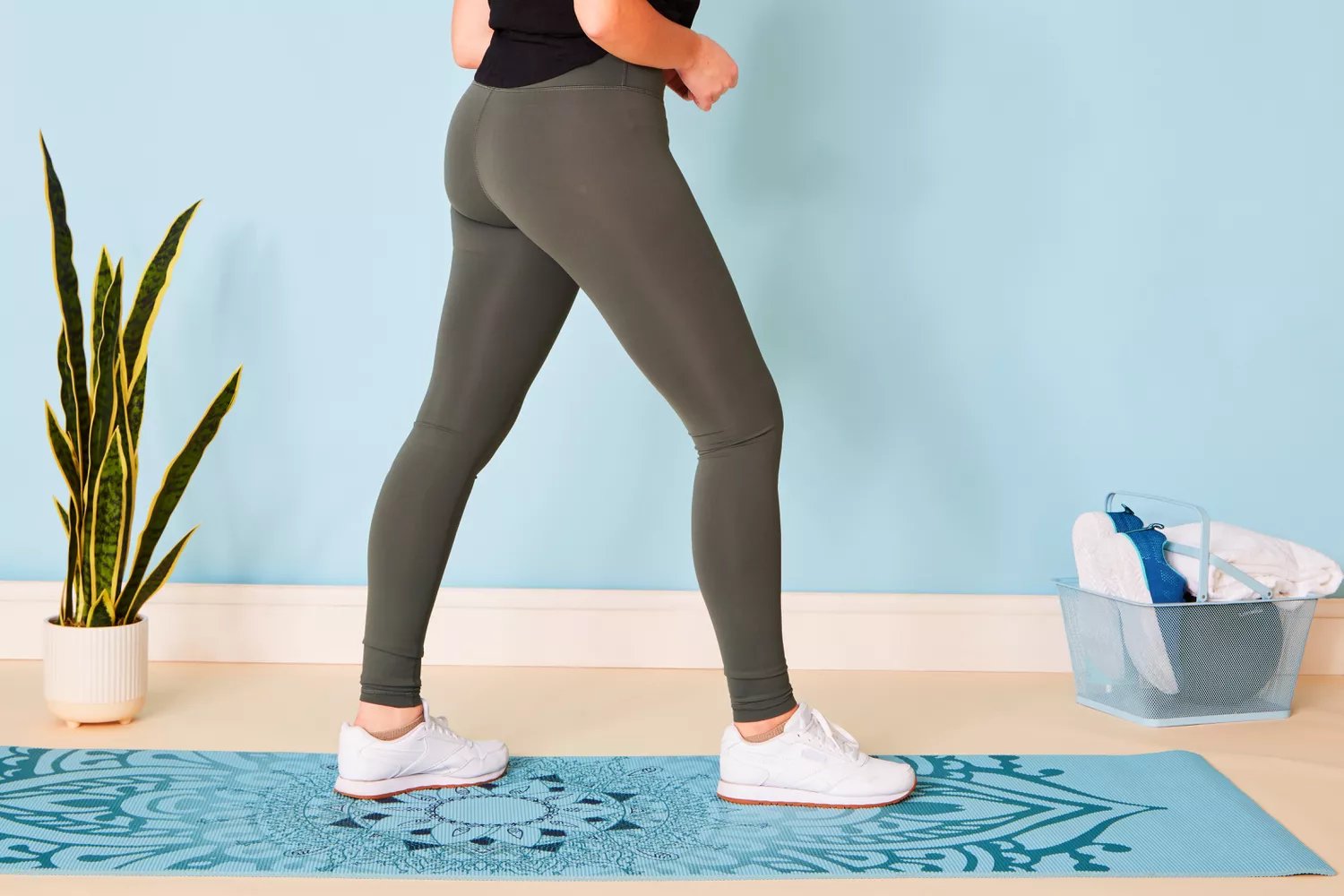 A woman performing a walking lunge on a yoga mat to test garment flexibility.