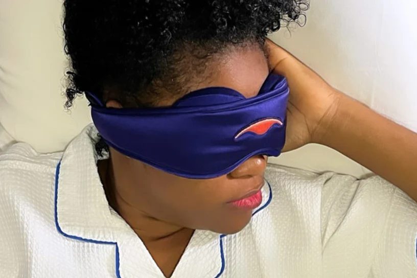 A woman wearing a blue silk sleep mask with built-in eye cups.