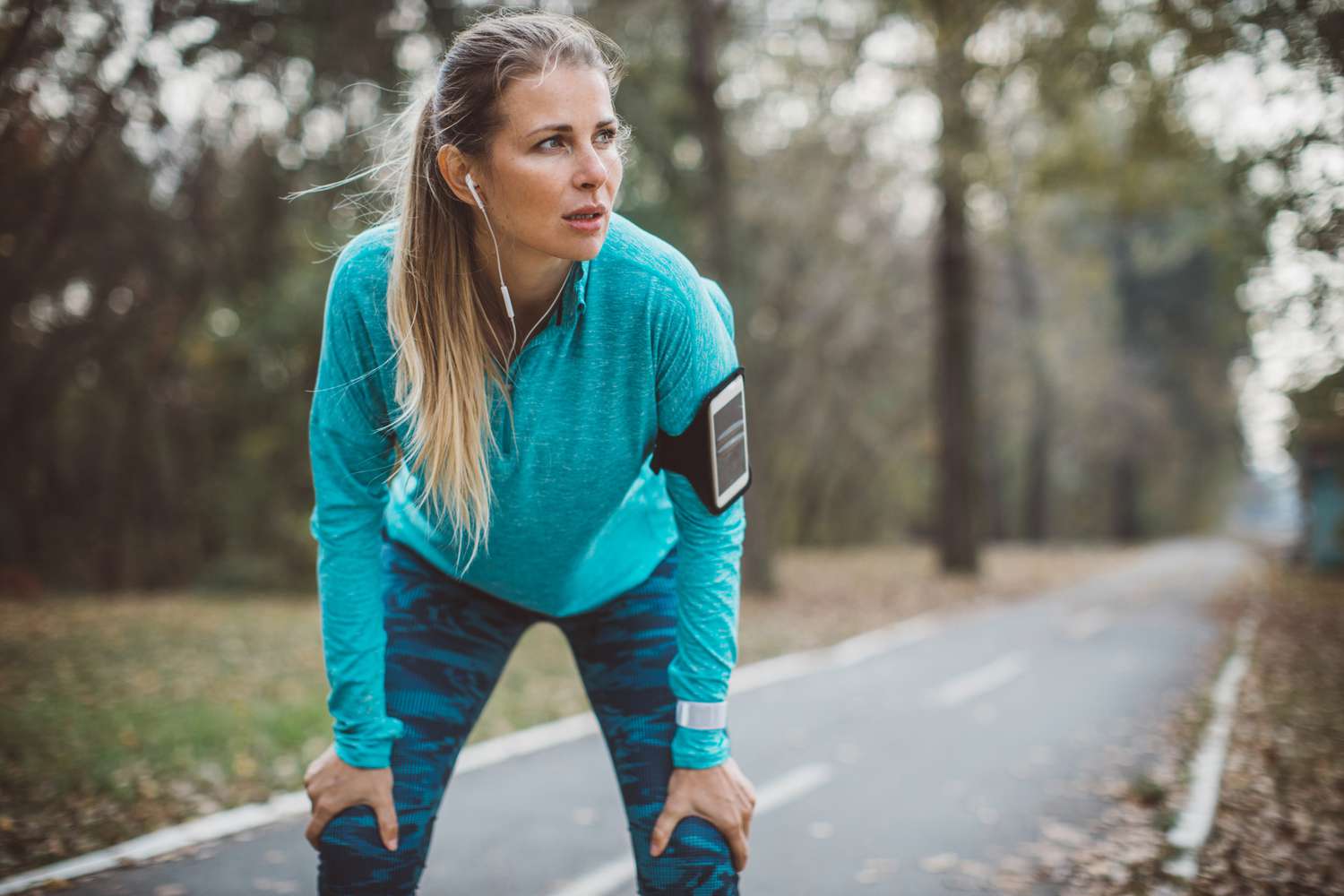 A female runner taking a planned rest break on a wooded path to recover during her workout.