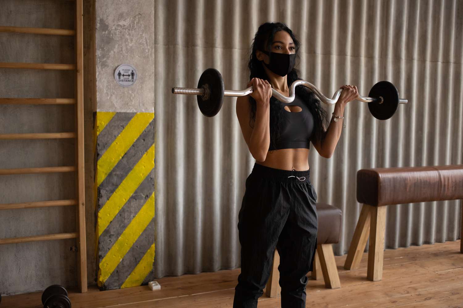 A Black woman lifting weights while wearing a face mask in a gym.