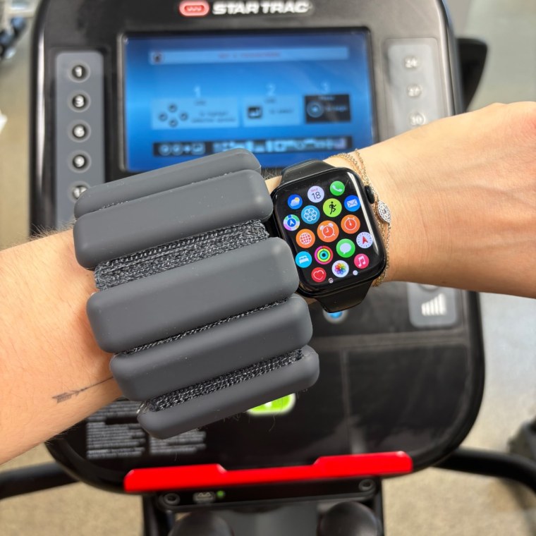 A person wearing a black Bala Bangle on their wrist alongside an Apple Watch.