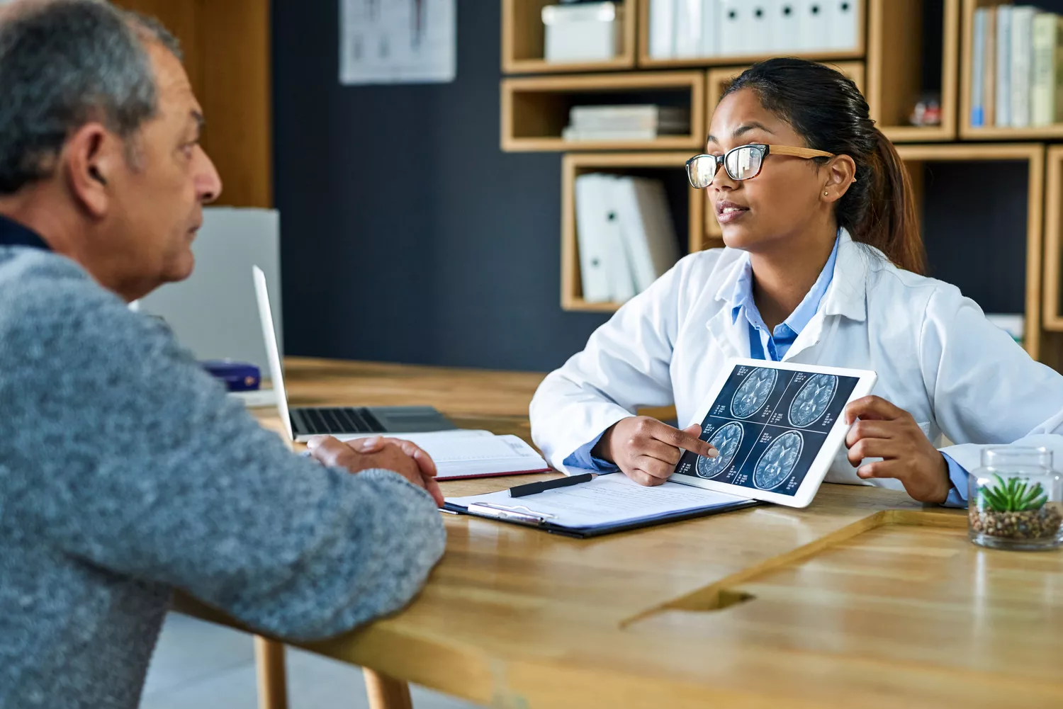A female doctor showing brain MRI scans on a tablet to an older male patient in a modern clinic.