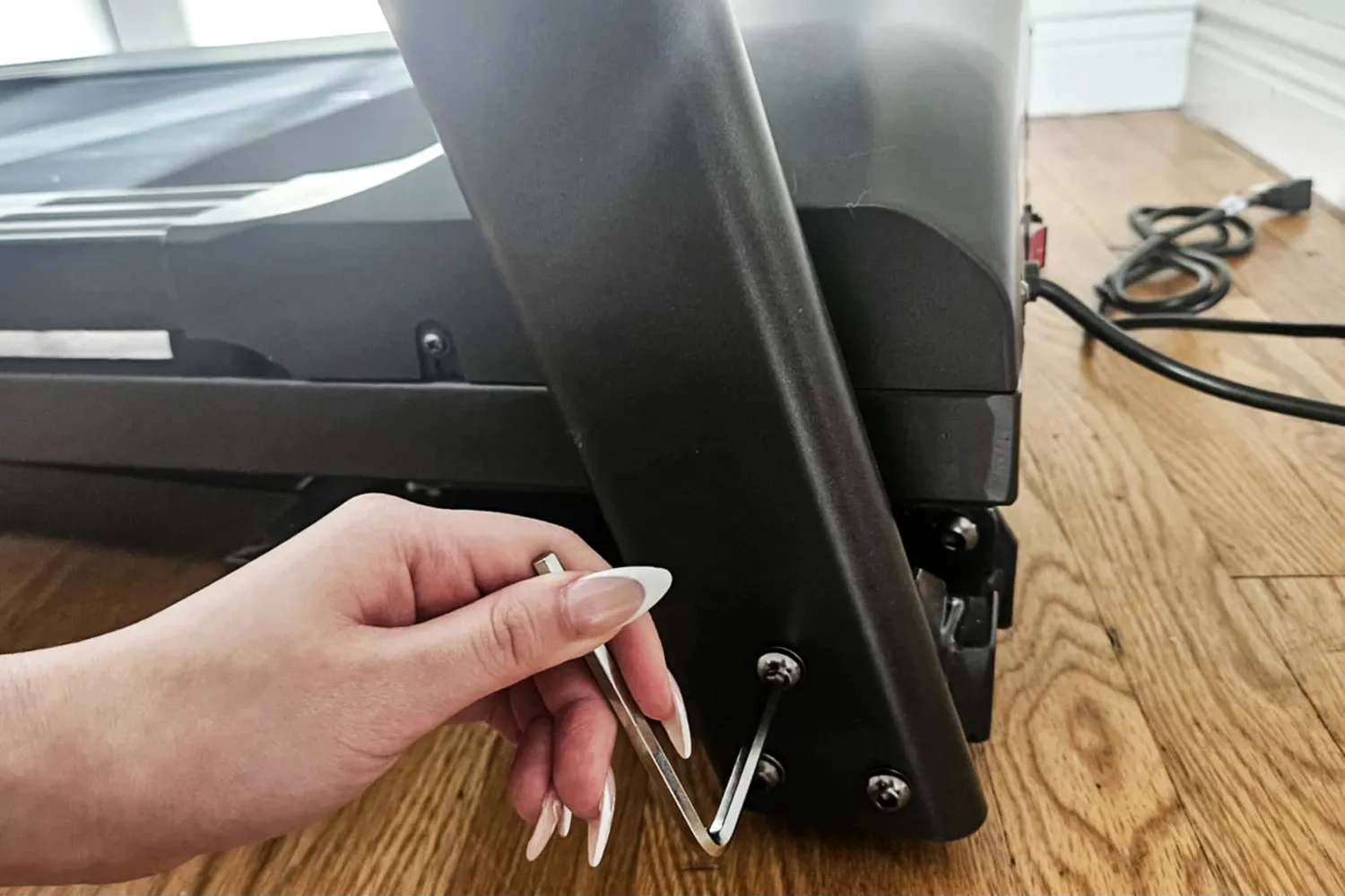 A person using an Allen key to adjust a screw on the base of a treadmill.