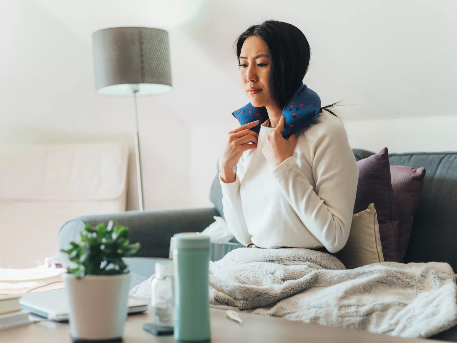 A woman applying a heating pad to her shoulder for comfort.