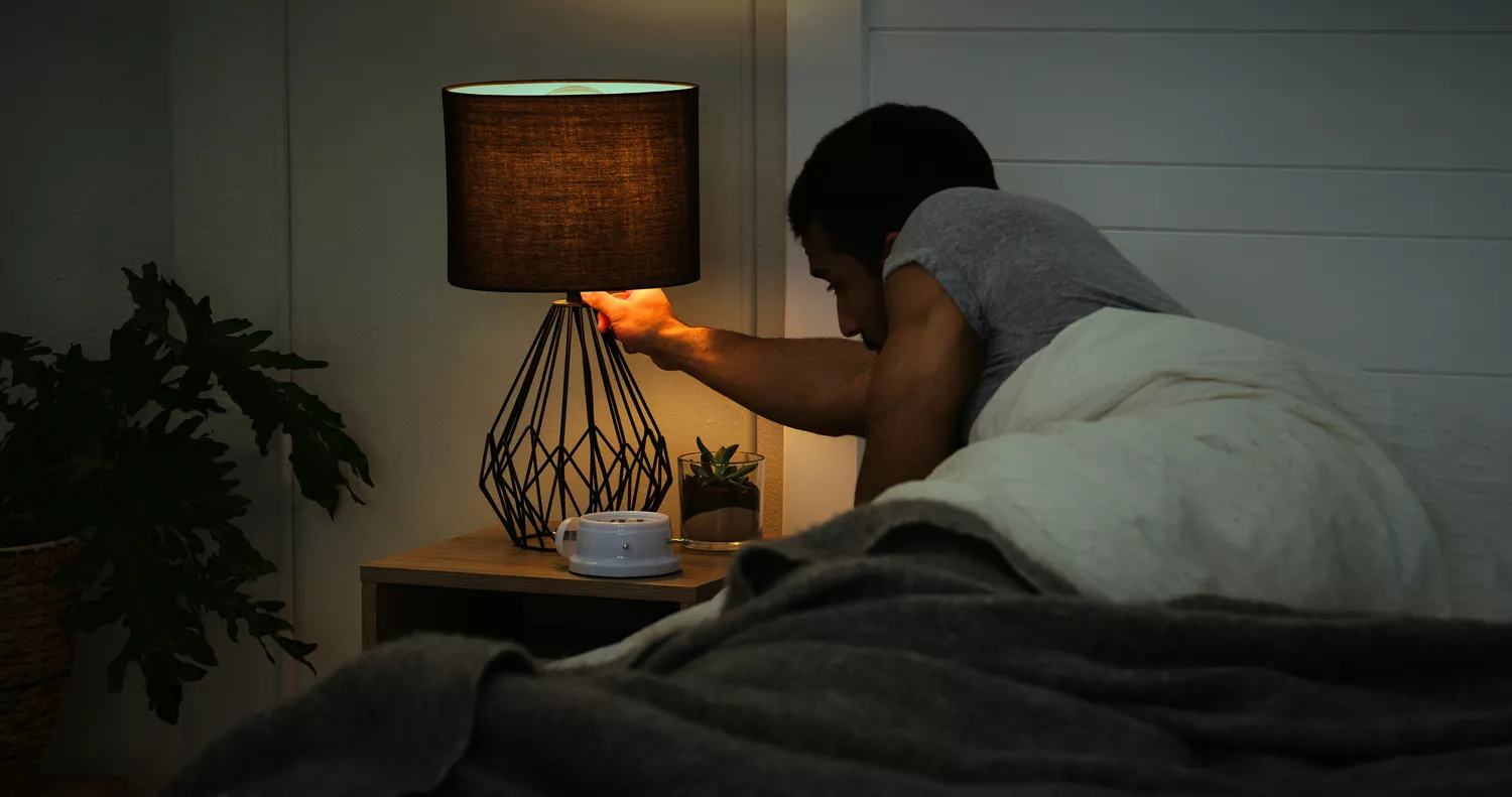 A person in a bedroom environment turning off a lamp to prepare for sleep.