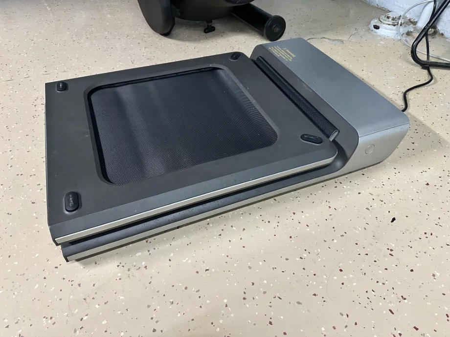 A WalkingPad treadmill in its fully folded position on the floor.