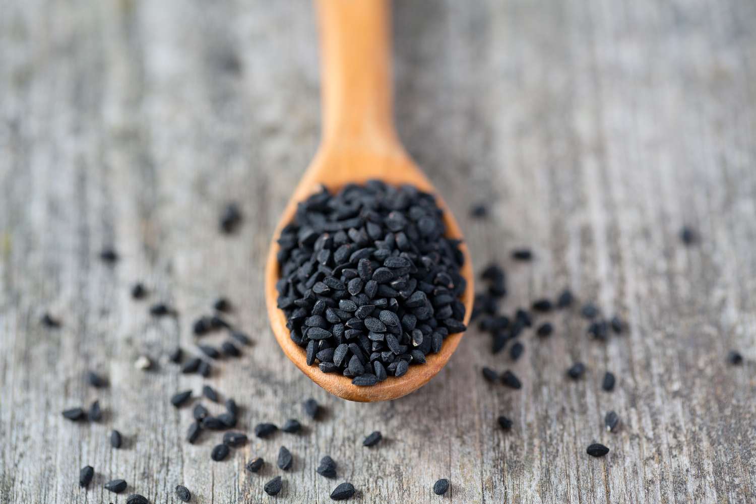 Raw black cumin seeds scattered on a natural wooden surface.