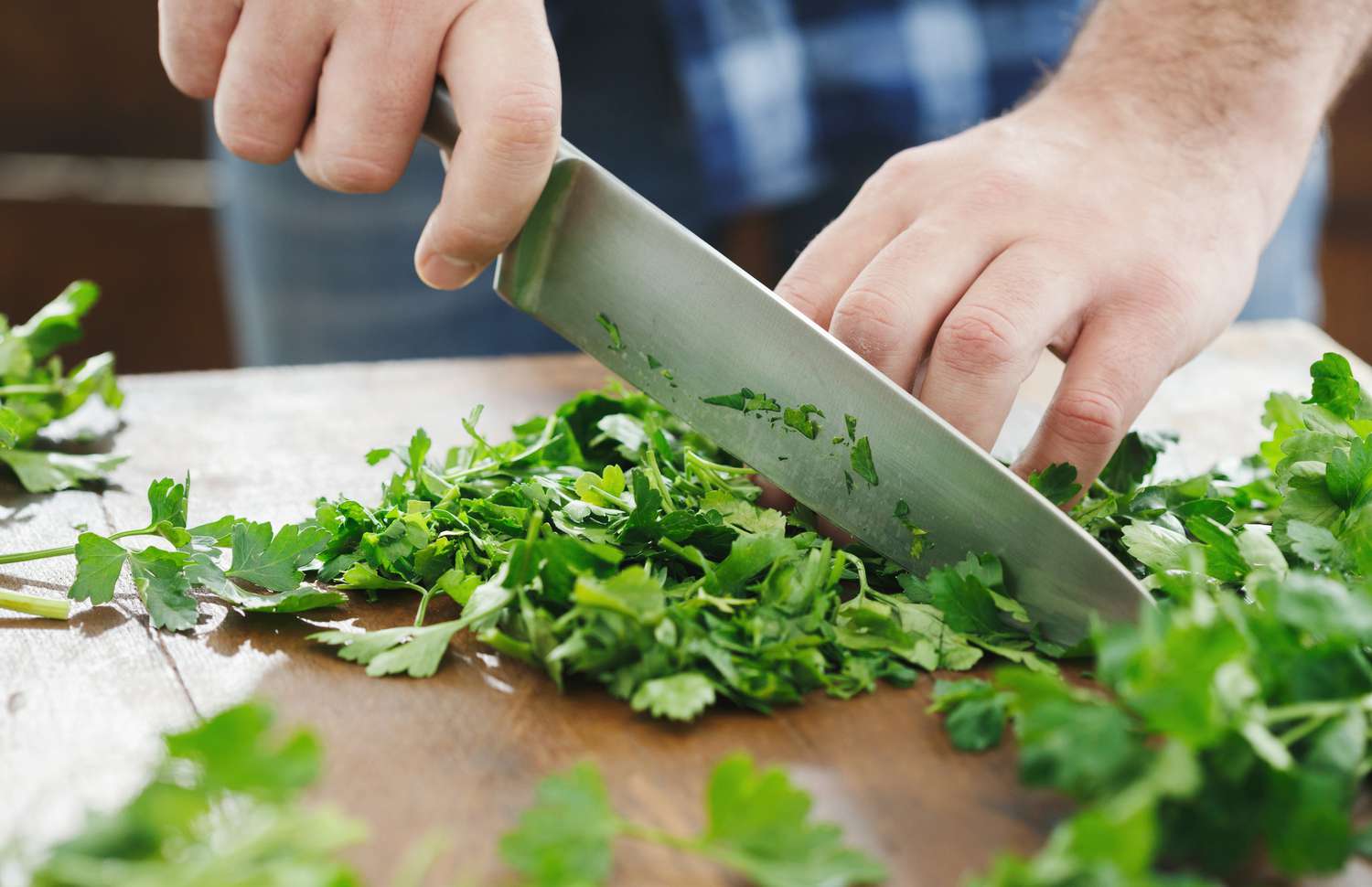 Close-up of a person's hands chopping fresh cilantro on a rustic wooden cutting board.