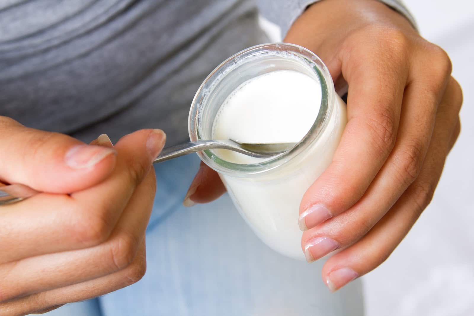 Close-up of a person holding a small jar of fresh white yogurt with a spoon.