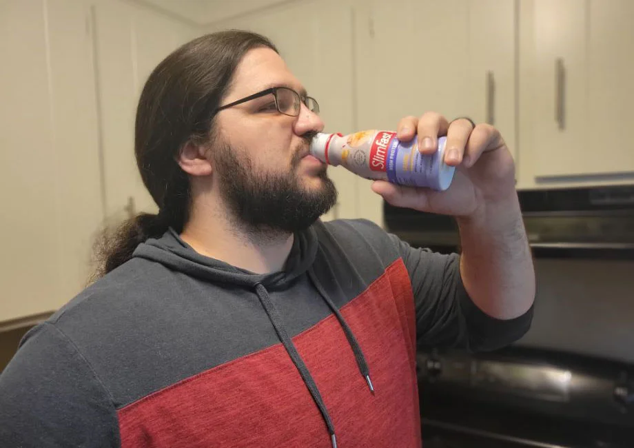 A person drinking a protein shake from a shaker bottle in a casual setting.