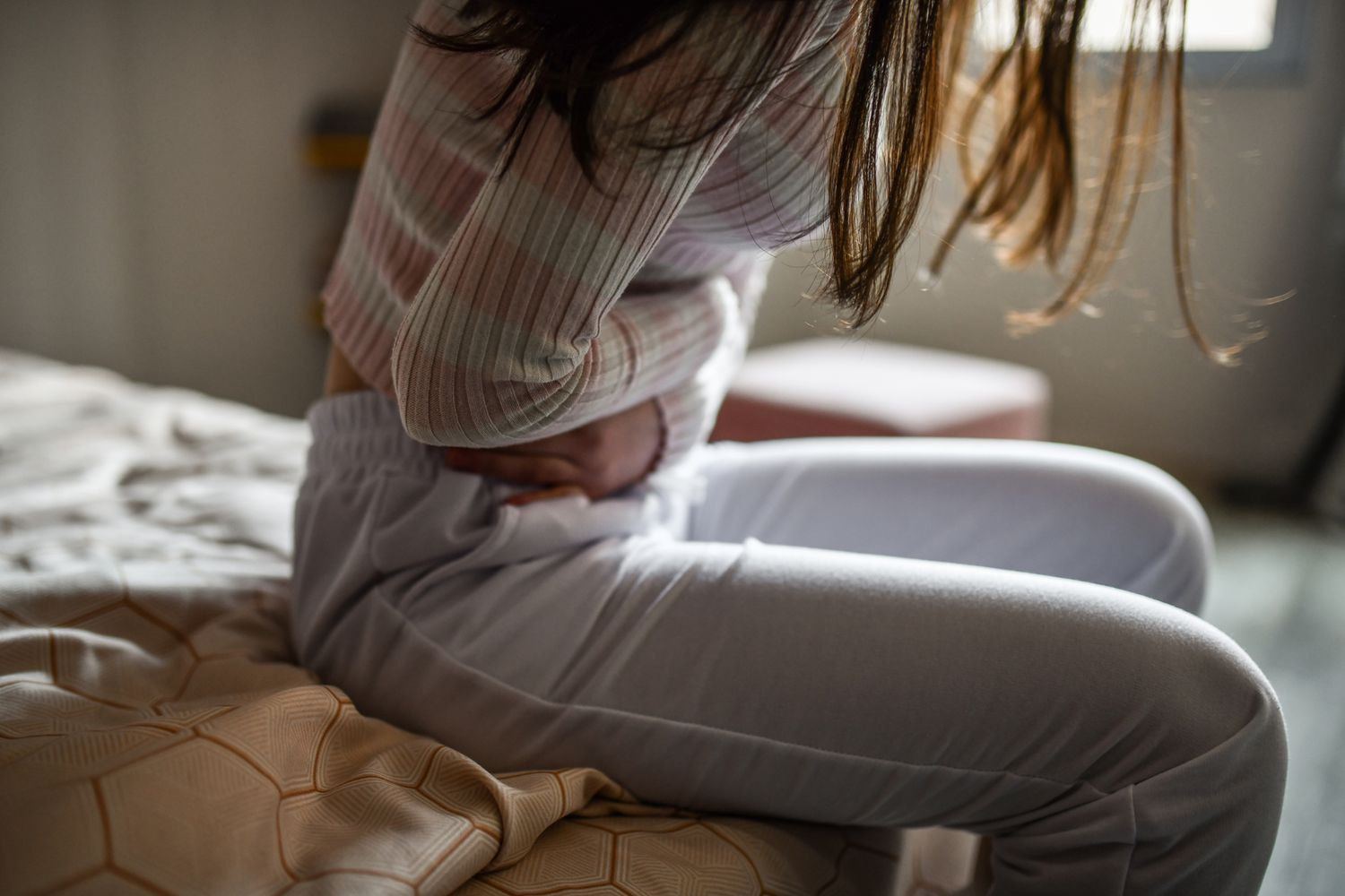 A woman sitting on a bed clutching her abdomen in pain.