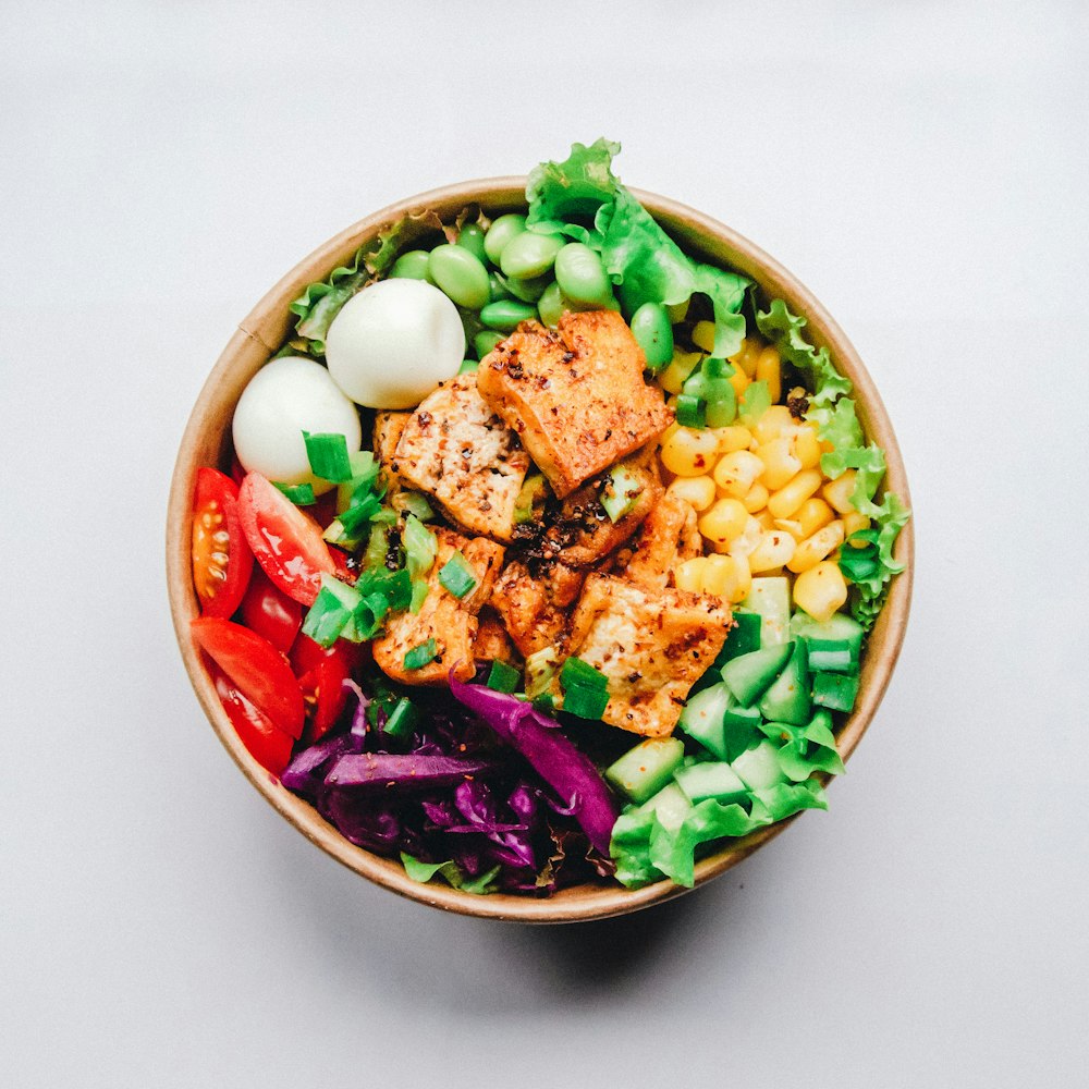 A healthy bowl containing grilled chicken, avocado, and leafy greens.