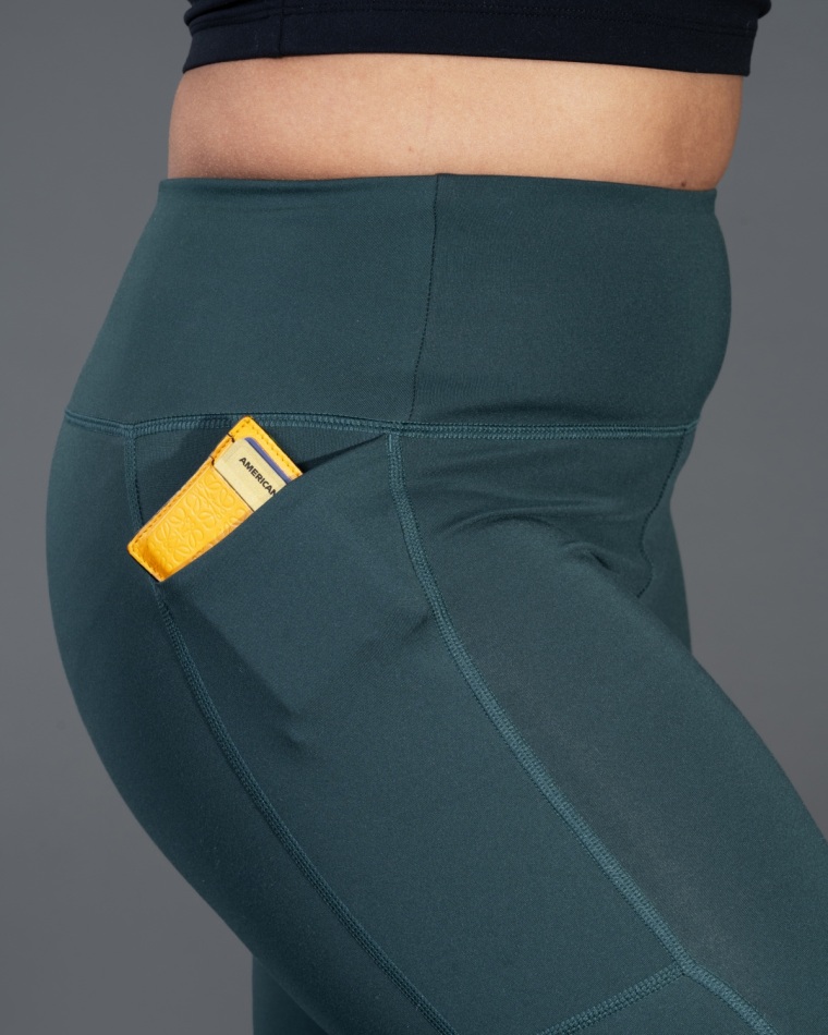 A hand sliding a smartphone into a deep side pocket on a pair of blue athletic leggings.