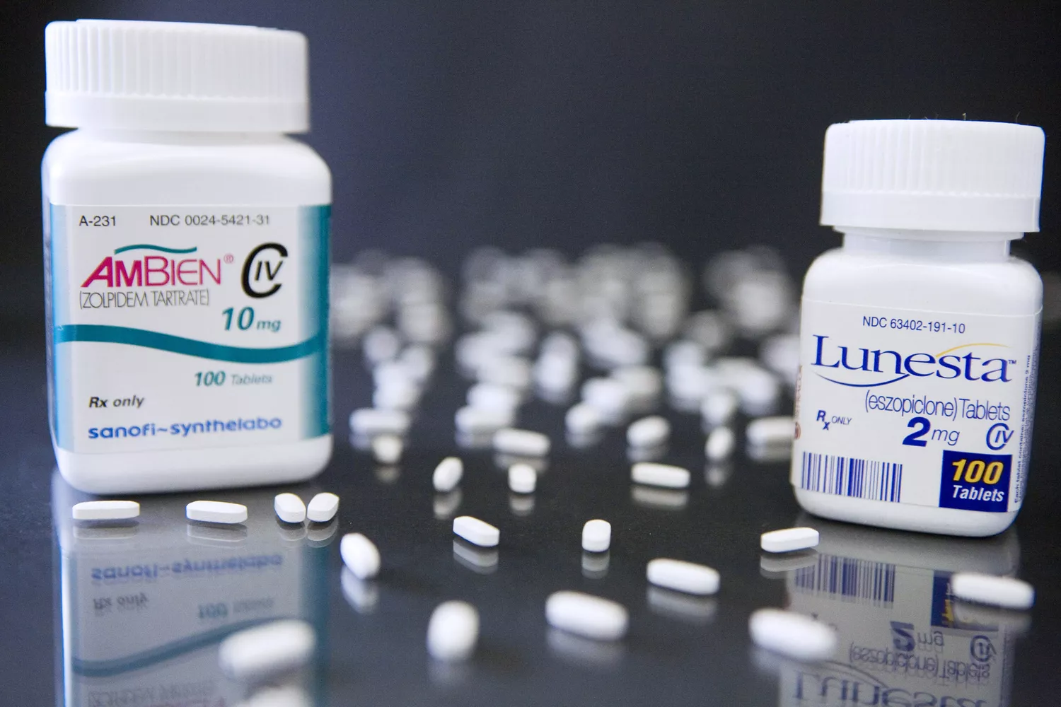 Prescription pill bottles and tablets of Ambien and Lunesta displayed in a professional pharmacy environment.