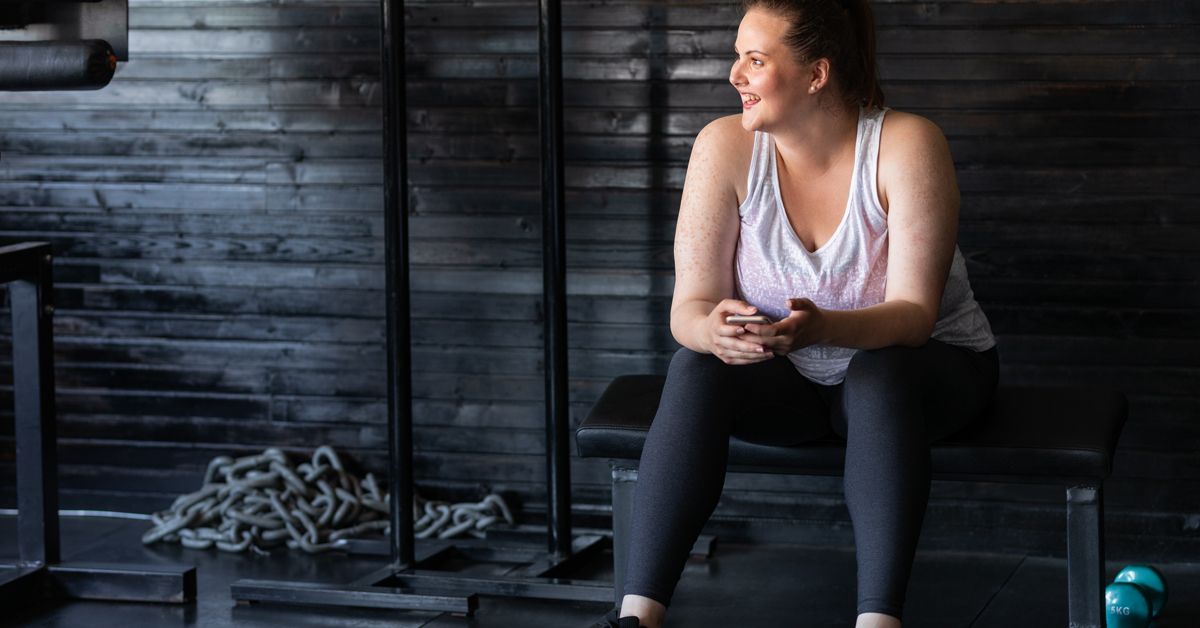 A fitness enthusiast taking a rest break on a weight bench in a modern gym setting.