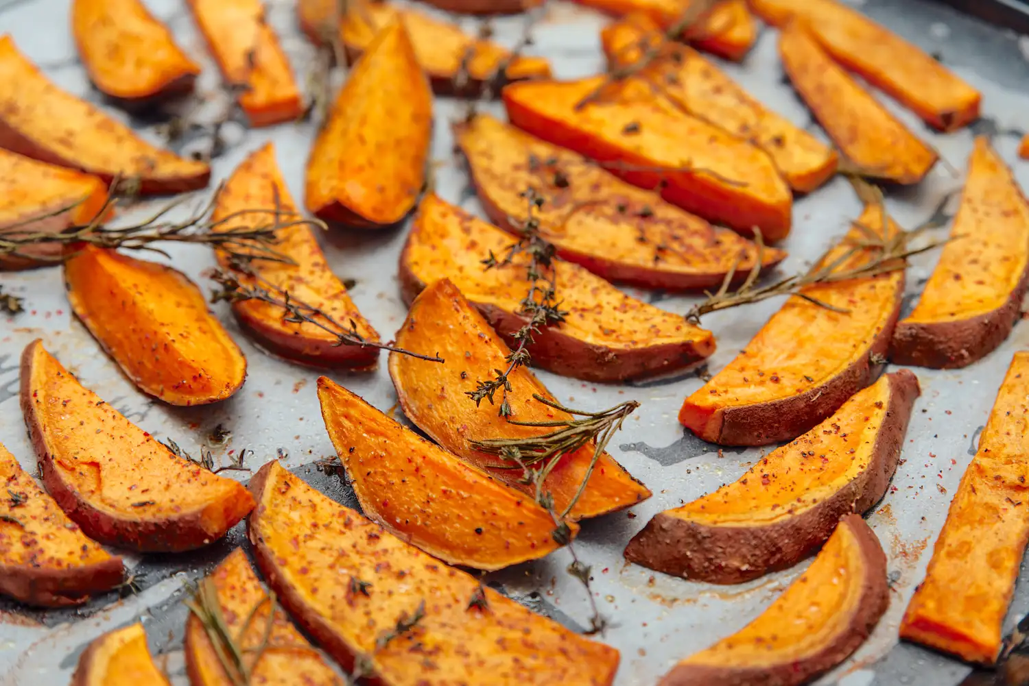 Roasted sweet potato wedges with fresh thyme on a baking sheet.