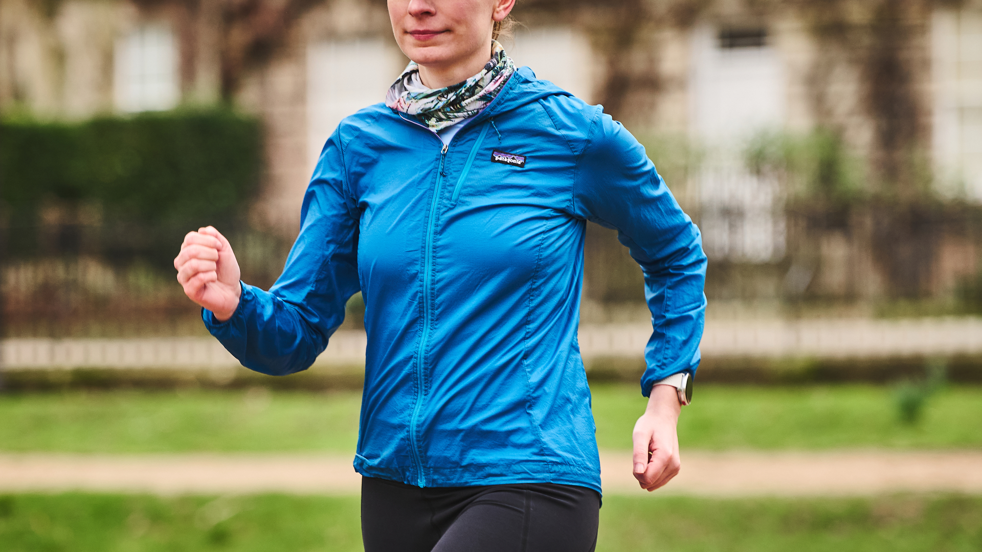 A woman running on a trail wearing a Patagonia Houdini jacket.