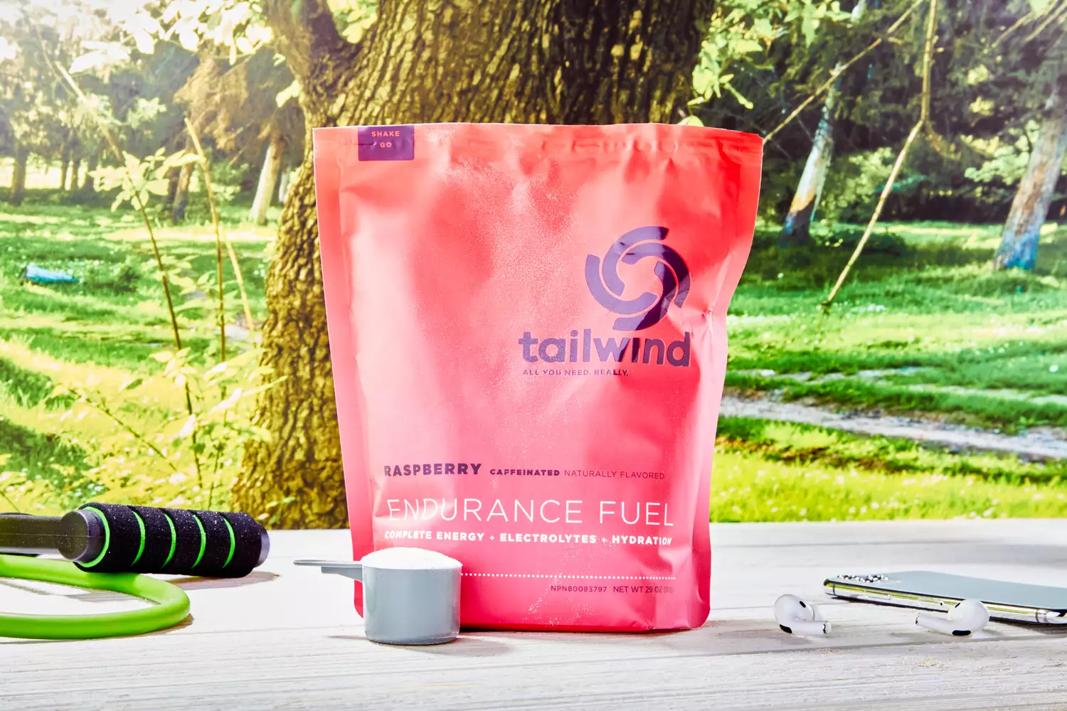 A bag of Tailwind Raspberry Caffeinated Endurance Fuel outdoors next to a jump rope and earbuds.