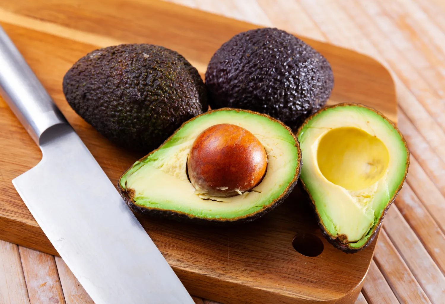Fresh avocados cut in half on a wooden board.