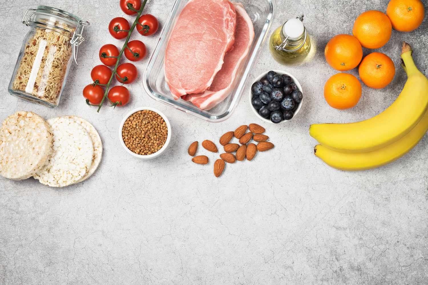Flat-lay arrangement of fresh pork, grains like buckwheat, and low FODMAP fruits and nuts.
