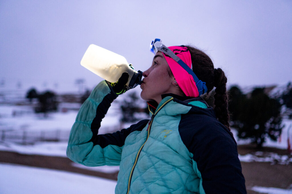 A female skimo athlete fueling with a recovery drink outdoors.