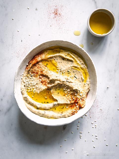 Extreme close-up of a smooth, creamy hummus swirl topped with olive oil and red spices.