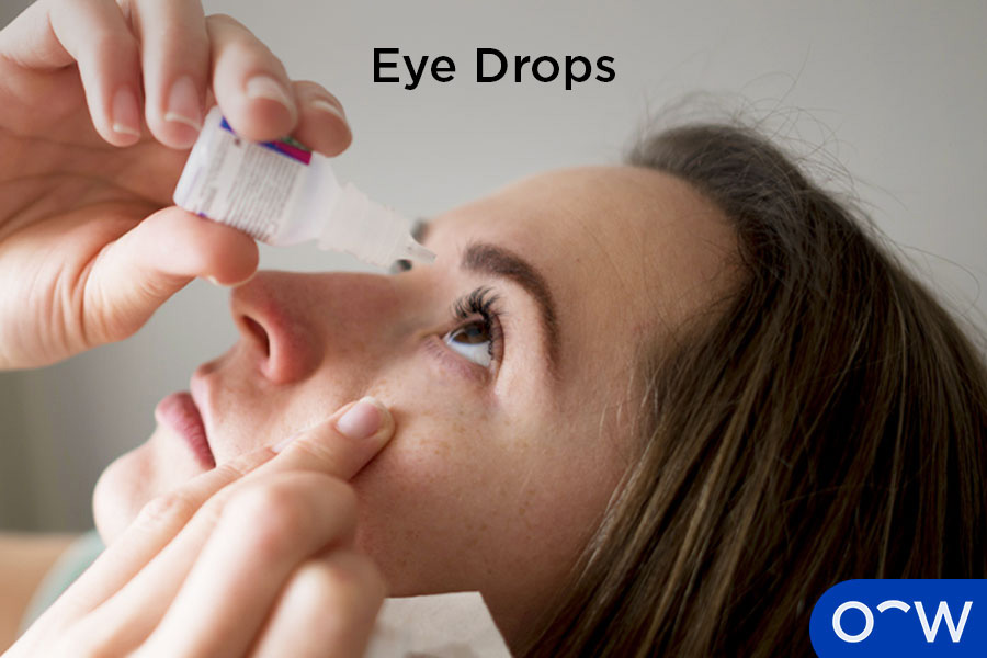 A woman carefully applying lubricating eye drops to her eye to relieve dryness.