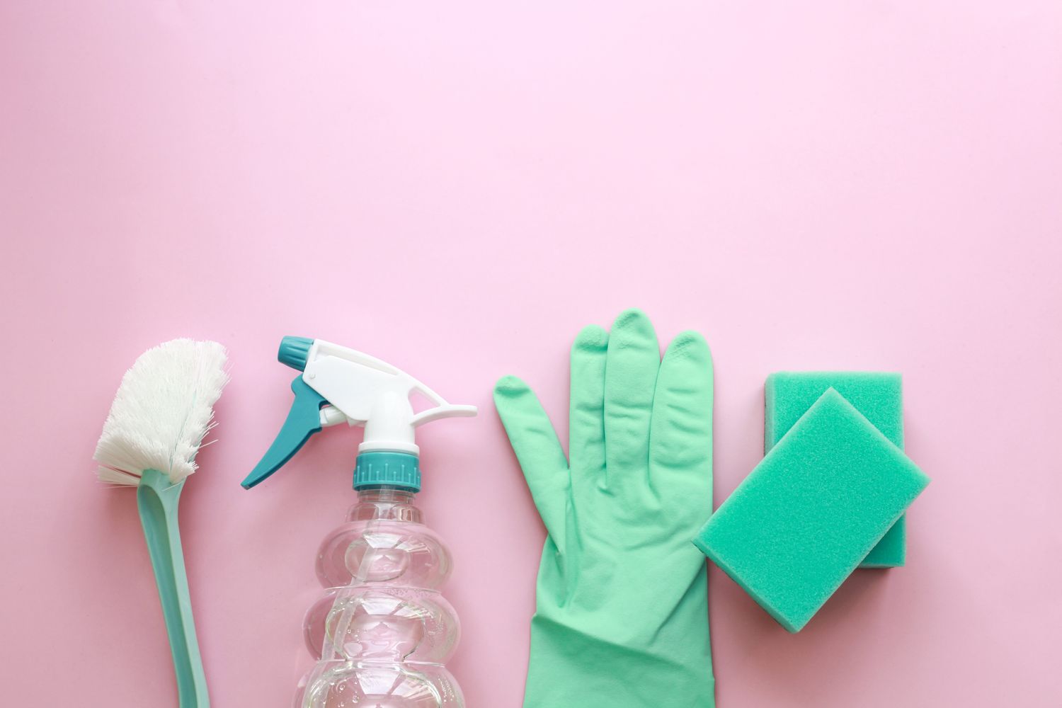 A collection of cleaning supplies including a spray bottle and sponges against a bright pink background.