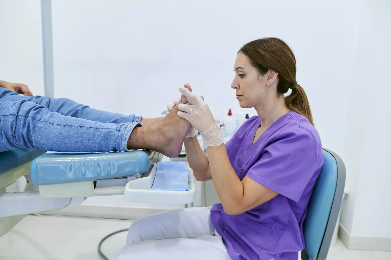 A podiatrist wearing gloves examines a patient's foot in a clinical setting.