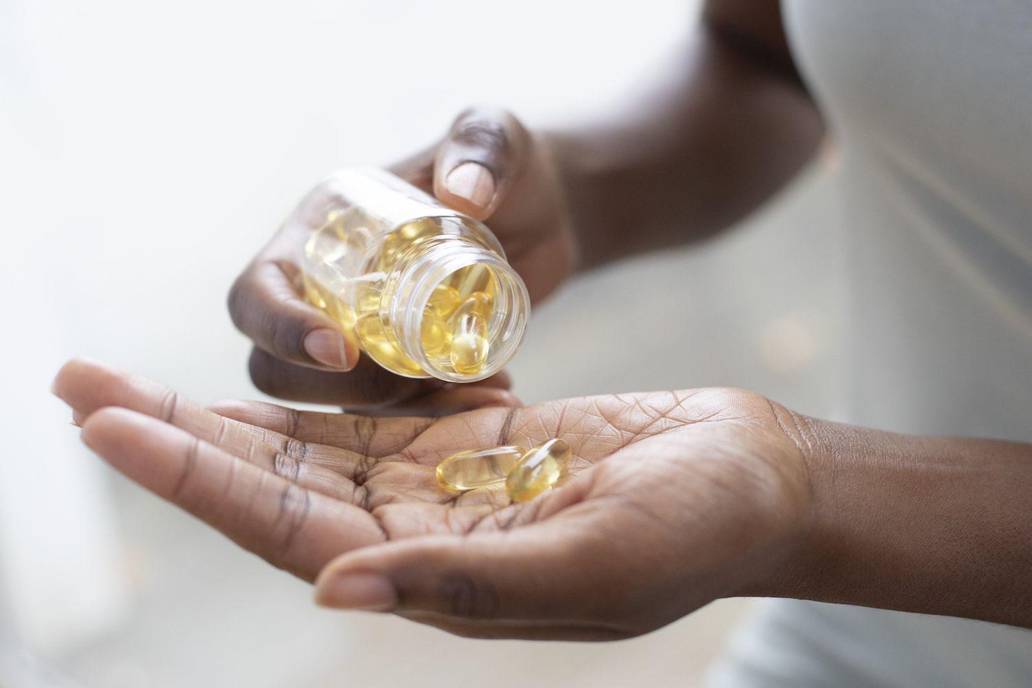 A close-up of a person holding several golden oil-filled supplement capsules in their palm.