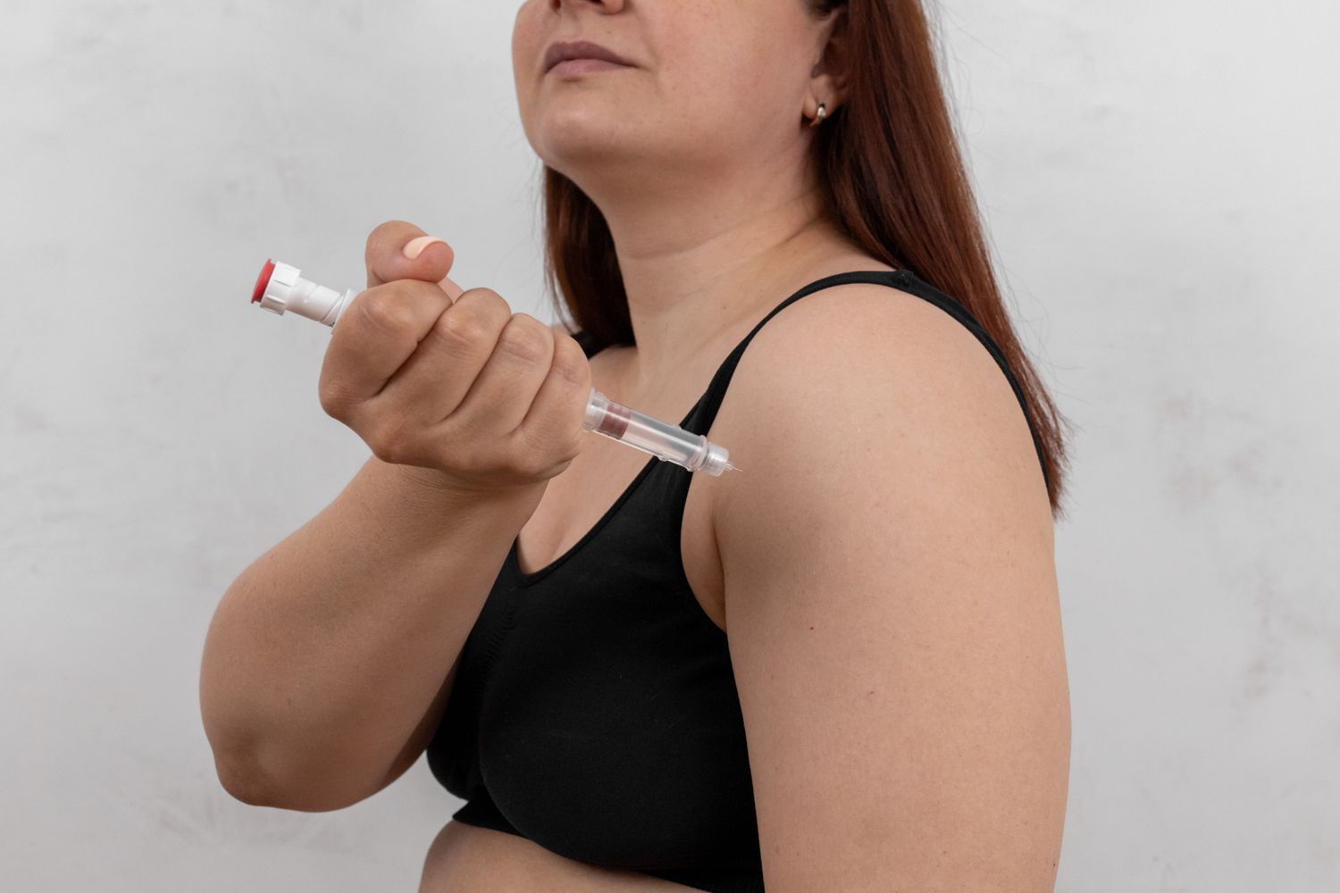 A person administering a medical injection into their arm.