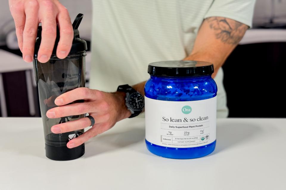 Close-up of a person adding powder into a shaker bottle to prepare a plant-based protein drink.