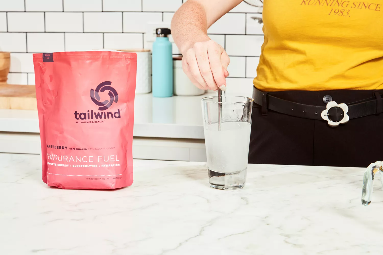 A person stirring a raspberry-flavored caffeinated supplement into a glass of water on a kitchen counter.