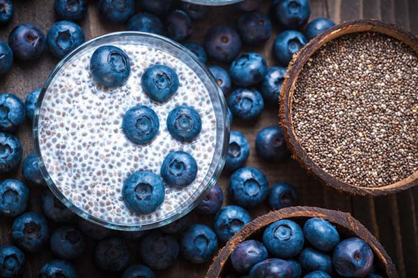 Overhead view of dry chia seeds next to chia pudding soaking in almond milk with blueberries.